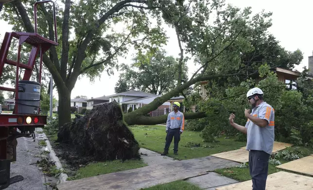 Workers cleared an uprooted tree from a lawn in Norridge, Ill., Tuesday, July 16, 2024. The tree was toppled as storms with reports of tornadoes blew through Iowa, Illinois and Indiana. (AP Photo/Teresa Crawford)