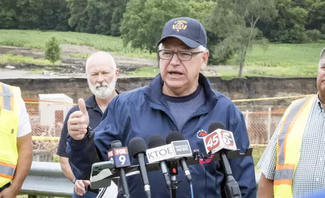 Minnesota Gov. Tim Walz addresses media members Tuesday, July 2, 2024, at the Rapidan Dam, in Rapidan, Minn. Rushing waters from the Blue Earth River have already left a trail of debris and destruction on the edges of a southern Minnesota dam that partially failed last week. (Casey Ek/The Free Press via AP)