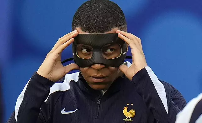 FILE - Kylian Mbappe of France adjusts his face mask as the team warms-up before the Group D match between the Netherlands and France at the Euro 2024 soccer tournament in Leipzig, Germany, on June 21, 2024. Kylian Mbappé has had more masks than goals at Euro 2024. Widely regarded as the heir to Lionel Messi and Cristiano Ronaldo as soccer's biggest icon, the France striker is struggling with his peripheral vision due to the protective face covering he has been fitted with since breaking his nose at the start of the European Championship.(AP Photo/Hassan Ammar)