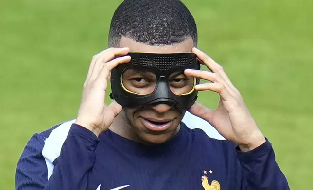 FILE - France's Kylian Mbappe gestures as he adjusts his face mask during a training session in Paderborn, Germany, on June 27, 2024. Kylian Mbappé has had more masks than goals at Euro 2024. Widely regarded as the heir to Lionel Messi and Cristiano Ronaldo as soccer's biggest icon, the France striker is struggling with his peripheral vision due to the protective face covering he has been fitted with since breaking his nose at the start of the European Championship. (AP Photo/Hassan Ammar)