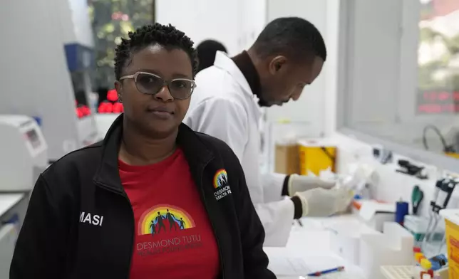 Clinical trials co-ordinator Thandeka Nkosi, poses for a photo as lab technician Xolile Mhlanga, who works with vials of the anti-HIV drug lenacapavir, works in the background at the Desmond Tutu Health Foundation's Masiphumelele Research Site, in Cape Town, South Africa, Tuesday, July 23, 2024. (AP Photo/Nardus Engelbrecht)