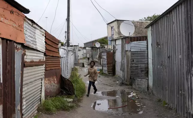 A child makes their way through drenched passages in Khayelitsha, Cape Town, South Africa, Thursday July 11, 2024. The South African city of Cape Town and surrounding areas have been hit by more storms, ripping roofs off houses and causing widespread flooding. (AP Photo/Nardus Engelbrecht)
