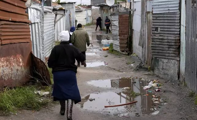 People make their way through drenched passages in Khayelitsha, Cape Town, South Africa, Thursday July 11, 2024. The South African city of Cape Town and surrounding areas have been hit by more storms, ripping roofs off houses and causing widespread flooding. (AP Photo/Nardus Engelbrecht)