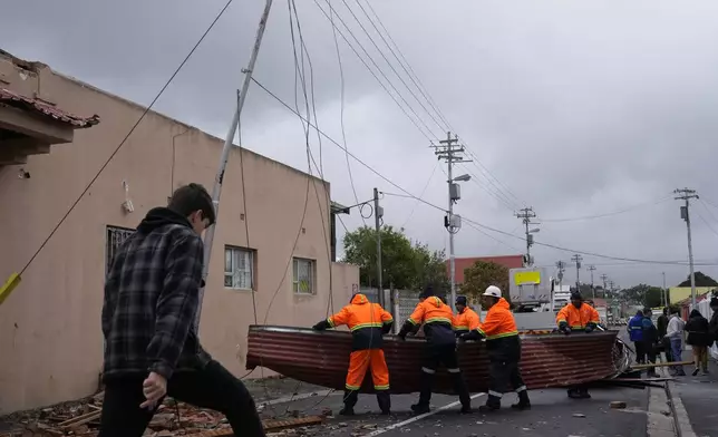 Rescue workers among damaged buildings in the Wynberg neighborhood of Cape Town, South Africa, Thursday, July 11, 2024. The area was hit overnight during strong winds that blew off roofs, destroyed parts of houses and other buildings, and brought down electricity poles. (AP Photo/Nardus Engelbrecht)
