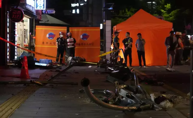 Rescuers stand near wreckage at the site of a car accident near Seoul City Hall in downtown Seoul, South Korea, Monday, July 1, 2024. A car hit pedestrians waiting at a traffic light in central Seoul on Monday evening, killing nine people and injuring four, South Korea's emergency officials said. (AP Photo/Ahn Young-joon)