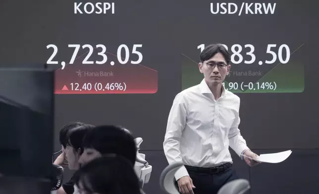 A currency trader passes by the screen showing the Korea Composite Stock Price Index (KOSPI), left, and the foreign exchange rate between U.S. dollar and South Korean won at the foreign exchange dealing room of the KEB Hana Bank headquarters in Seoul, South Korea, Friday, July 26, 2024. (AP Photo/Ahn Young-joon)