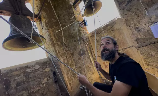 Sitting in a chair with ropes looped around both feet and hands, Joan Carles Osuna, a student of the Vall d'en Bas School of Bell Ringers, performs playing all four bronze bells at the church bell tower of the12th-century Sant Romà church, at the village of Joanetes, about two hours north of Barcelona, Spain, Saturday, July 29, 2024. A school set up to revive the manual ringing of church bells has graduated its first class of 18 students after learning their ringing skills. (AP Photo/Emilio Morenatti)