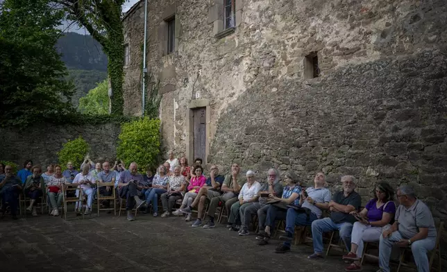 Local people sit around the12th-century Sant Romà church as they listen the students of the Vall d'en Bas School of Bell Ringers playing bells, in the tiny village of Joanetes about two hours north of Barcelona, Spain, Saturday, July 29, 2024. A school set up to revive the manual ringing of church bells has graduated its first class of 18 students after learning their ringing skills. (AP Photo/Emilio Morenatti)