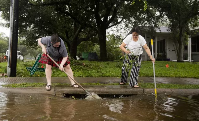 Louise Cohen, right, and Zilfa Ruhen help clear neighborhood drains after Beryl made landfall early morning Monday, July 8, 2024, in Houston. The National Hurricane Center said damaging winds and flash flooding will continue as Beryl continues pushing inland. (Ishika Samant/Houston Chronicle via AP)