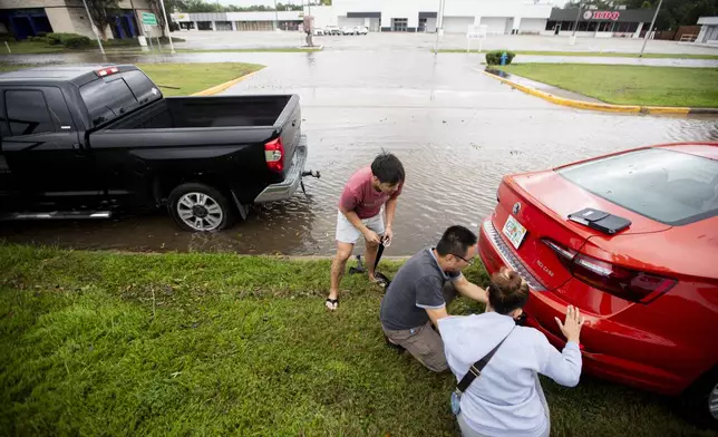 Anthony Le, left, and his father Phuong Le help pull a car stuck in the mud after Beryl made landfall early morning Monday, July 8, 2024, in Houston. The National Hurricane Center said damaging winds and flash flooding will continue as Beryl continues pushing inland. (Ishika Samant/Houston Chronicle via AP)