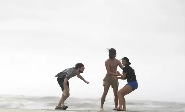 Beach goers try to keep their balance as wind gusts continue as Tropical Storm Beryl wanes on Monday, July 8, 2024, Galveston, Texas. (Elizabeth Conley/Houston Chronicle via AP)