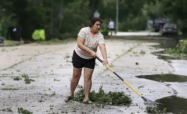 Resident Isabel Perez rakes up downed tree branches from the street outside of her home during a lull in the wind and rain as Tropical Storm Beryl passes Monday, July 8, 2024, in Rosenburg, Texas. Hurricane Beryl has been downgraded to a tropical storm after sweeping into Texas as a Category 1 storm with heavy rains and powerful winds. (AP Photo/Michael Wyke)