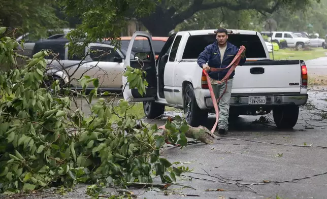 William Ruiz uses a tow strap and his pick-up truck to remove a downed tree branch from the middle of the street in his neighborhood during a lull as the eye of hurrican Beryl passes through Monday, July 8, 2024, in Rosenberg, Texas. (AP Photo/Michael Wyke)