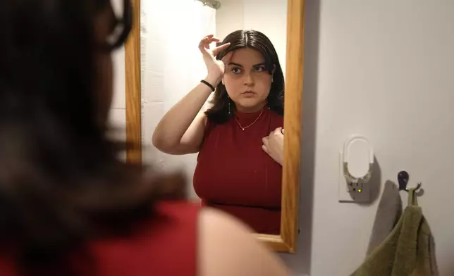 Daniella López White, of Hawaii, uses a mirror while adjusting her hair, Tuesday, May 14, 2024, at her apartment, in Boston. López White, who graduated from Emerson College in Boston this month and is on a tight budget, said TikTok influencers have helped her with tips on how to find affordable clothes at places like H&amp;M and thrift shops. (AP Photo/Steven Senne)