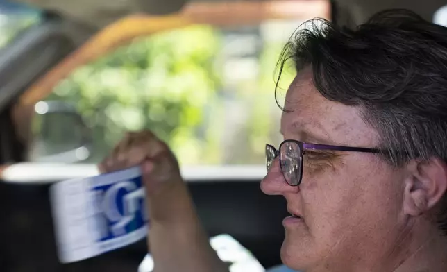 Sherri Thompson uses her disability parking sign to fan off as she waits for the Cook Plaza cooling center to open on Friday, July 5, 2024, in Gresham, Ore. Thompson has lived in her car for three years, and can only run its air conditioning for about 20 minutes at a time as it causes the engine to overheat. A heat wave is spreading across Wester U.S., the national Weather Service said, sending many residents in search of a cool haven from the dangerously high temperatures. (AP Photo/Jenny Kane)