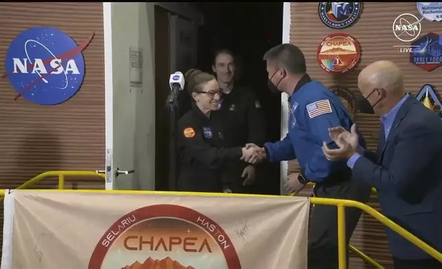 In this image made from video provided by NASA, the crew members of the first CHAPEA mission, Kelly Haston, center, shakes hands with NASA Deputy Director Flight Missions Kjell Lindgren, second right, as other crew Ross Brockwell, emerges from their craft, Saturday, July 6, 2024, at Johnson Space Center in Houston, Texas. The crew of a NASA mission to Mars emerged from their craft after a yearlong voyage that never left Earth. The four volunteers crew members spent more than 12 months inside NASA's first simulated Mars environment at Johnson Space Center in Houston, coming out of the artificial alien environment Saturday. (NASA via AP)