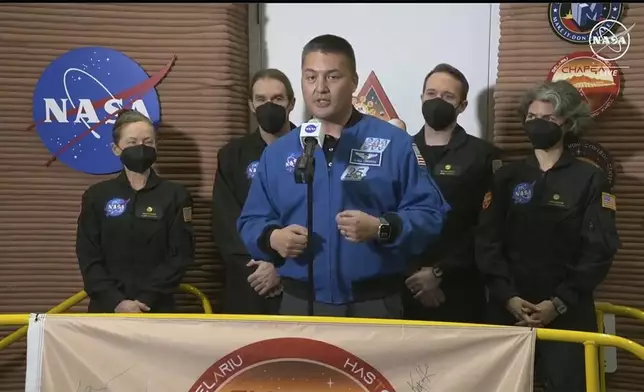 In this image made from video provided by NASA, NASA Deputy Director Flight Missions Kjell Lindgren, center, speaks in front of the crew members of the first CHAPEA mission, from left to right, Kelly Haston, Ross Brockwell, Nathan Jones, and Anca Selariu, after they emerged from their craft, Saturday, July 6, 2024, at Johnson Space Center in Houston, Texas. The crew of a NASA mission to Mars emerged from their craft after a yearlong voyage that never left Earth. (NASA via AP)