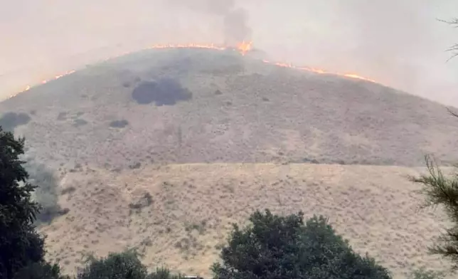 In this photo provided by Alison Oszman, a fast-moving wildfire near the Orego-Idaho border moves toward a home on Rye Valley Lane in Huntington, Ore., in the afternoon o fWednesday, July 24, 2024. (Alison Oszman via AP Photo)