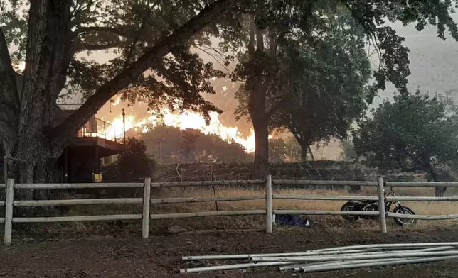 In this photo provided by Alison Oszman, a fast-moving wildfire near the Orego-Idaho border moves toward a home on Rye Valley Lane in Huntington, Ore., in the afternoon o fWednesday, July 24, 2024. (Alison Oszman via AP Photo)