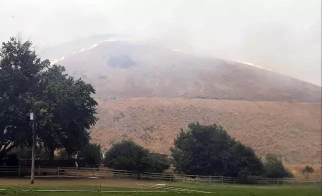 In this photo provided by Alison Oszman, a fast-moving wildfire near the Orego-Idaho border moves toward a home on Rye Valley Lane in Huntington, Ore., in the afternoon o fWednesday, July 24, 2024. (Alison Oszman via AP Photo)