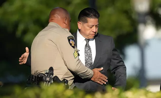 Former Uvalde Consolidated Independent School District police officer Adrian Gonzales, right, greets a Sheriff's deputy as he arrives at the Uvalde County Courthouse, Thursday, July 25, 2024, in Uvalde, Texas. Gonzales made his first court appearance on charges of abandoning and failing to protect children. (AP Photo/Eric Gay)