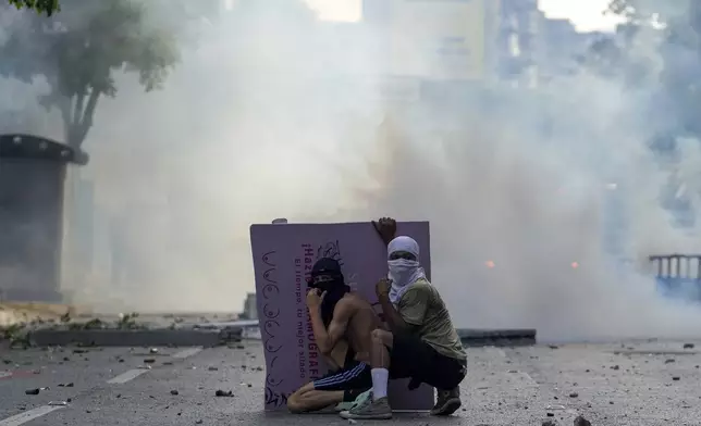 Protesters take cover during clashes with police in demonstrations against the official election results declaring President Nicolas Maduro's reelection, the day after the vote in Caracas, Venezuela, Monday, July 29, 2024. (AP Photo/Matias Delacroix)