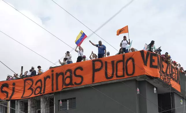 Supporters stand on the roof of a building adorned with a banner with a message that reads Spanish; "If Barinas could, Venezuela can" during a campaign rally for opposition presidential candidate Edmundo Gonzalez in Barinas, Venezuela, Saturday, July 6, 2024. (AP Photo/Ariana Cubillos)