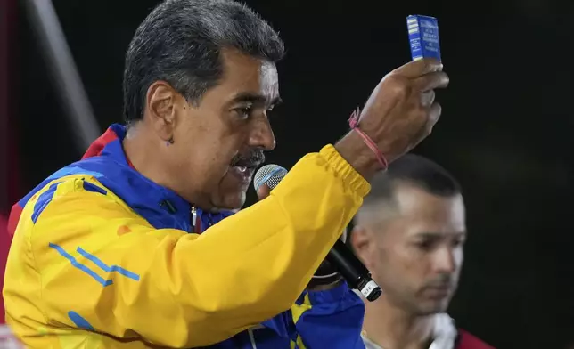 President Nicolas Maduro shows a mini edition of Venezuela's constitution as he addresses supporters gathered outside the Miraflores presidential palace after electoral authorities declared him the winner of the presidential election in Caracas, Venezuela, Monday, July 29, 2024. (AP Photo/Fernando Vergara)