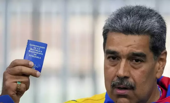 President Nicolas Maduro displays a mini edition of Venezuela's constitution after voting in the presidential elections in Caracas, Venezuela, Sunday, July 28, 2024. Maduro is seeking re-election for a third term. (AP Photo/Fernando Vergara)