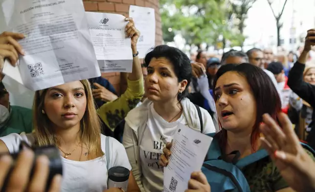 Opposition poll watchers display documents identifying themselves as such at the entrance to the Andres Bello School, the main polling station in Caracas, Venezuela, during the presidential elections on Sunday, July 28, 2024. (AP Photo/Cristian Hernandez)