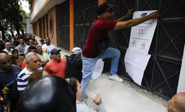 An electoral official posts polling station information as the opening of the polls for the presidential elections is delayed at the Andres Bello School, the main polling center in Caracas, Venezuela, Sunday, July 28, 2024. (AP Photo/Cristian Hernandez)