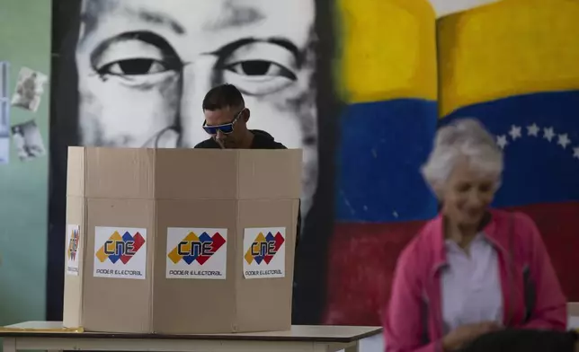 A man casts his ballot in front of a mural of President Hugo Chavez as part of a rehearsal for the July 28 presidential election at a voting center in Caracas, Venezuela, Sunday, June 30, 2024. (AP Photo/Cristian Hernandez Fortune)