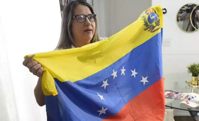 Yuly Macedo holds up a traditional seven-star Venezuelan flag that her son hangs in his room, different from the current eight-star flag that came to be under Hugo Chávez, during an interview in Davie, Florida, Thursday, July 11, 2024. Macedo, who now cleans houses in Miami, said that she has always opposed the government of Nicolas Maduro. In April 2016, she took a plane with her husband and her then 10-year-old son to Miami, where she requested political asylum and has lived ever since. (AP Photo/Wilfredo Lee)