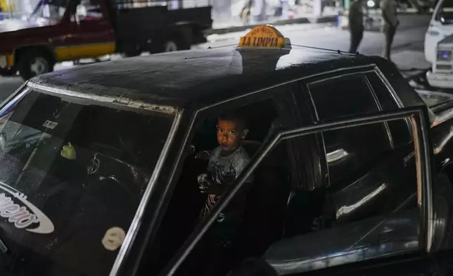 A boy waits for his father in a taxi near a flea market in Maracaibo, Venezuela, Monday, July 22, 2024. The country's presidential election is set for July 28. (AP Photo/Matias Delacroix)