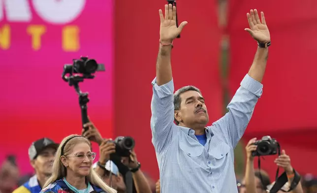 President Nicolas Maduro, accompanied by first lady Cilia Flores, raises his arms during his closing election campaign rally in Caracas, Venezuela, Thursday, July 25, 2024. Maduro is seeking a third term in the July 28 vote. (AP Photo/Fernando Vergara)