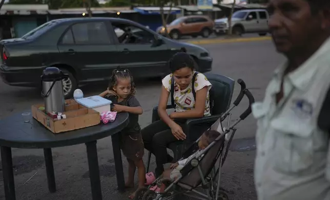 A woman with her children sells coffee near a bus station in Maturin, Venezuela, Saturday, July 20, 2024. The presidential election is set for July 28. (AP Photo/Matias Delacroix)