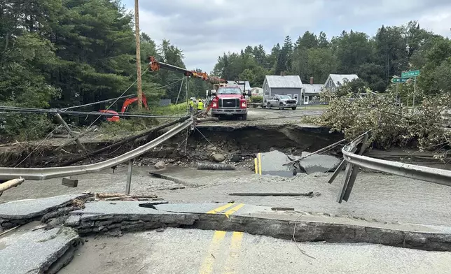 A crew works on a damaged roadway following flooding in Lyndonville, Vt., Tuesday, July 30, 2024. (AP Photo/Nick Perry)