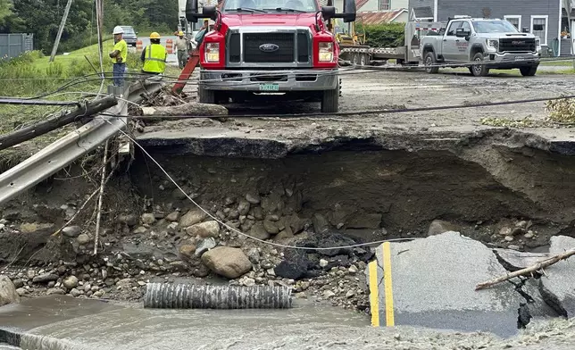 A crew works on a damaged roadway after flooding in Lyndonville, Vt., Tuesday, July 30, 2024. (AP Photo/Nick Perry)