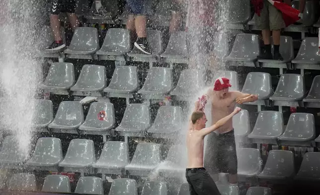 Fans dance in the rain as the round of sixteen match between Germany and Denmark at the Euro 2024 soccer tournament was suspended due to adverse weather in Dortmund, Germany, Saturday, June 29, 2024. (AP Photo/Hassan Ammar)