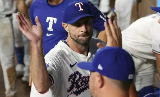 Texas Rangers starting pitcher Max Scherzer, center, gets high-fives in the dugout after pitching in the sixth inning against the Chicago White Sox in a baseball game Thursday, July 25, 2024, in Arlington, Texas. Scherzer exited the game with nine strikeouts for a career total of 3400. (AP Photo/Richard W. Rodriguez)