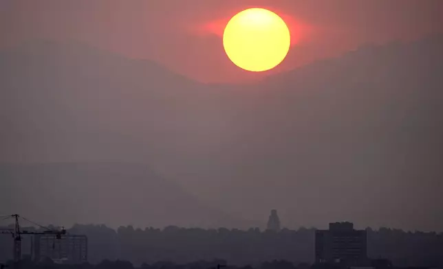 The sun sets behind the mountains obscured by wildfire smoke from blazes in the American West and provinces of western Canada late Wednesday, July 24, 2024, in Denver. (AP Photo/David Zalubowski)