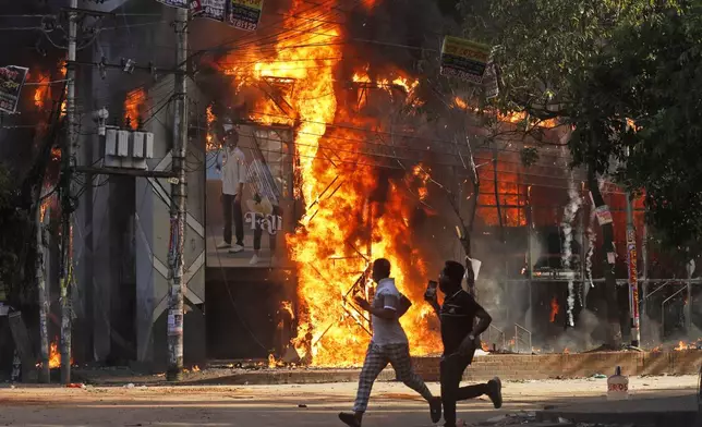 Men run past a shopping center which was set on fire by protesters during a rally against Prime Minister Sheikh Hasina and her government demanding justice for the victims killed in the recent countrywide deadly clashes, in Dhaka, Bangladesh, Sunday, Aug. 4, 2024. (AP Photo/Rajib Dhar)