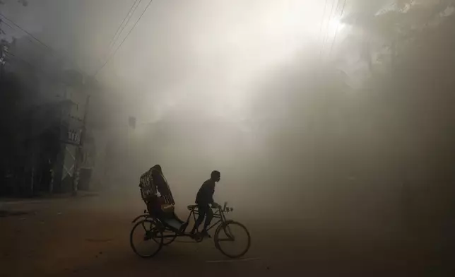 A rickshaw puller rides in the smoke caused by a burning shopping center which was set on fire by protesters during a rally against Prime Minister Sheikh Hasina and her government demanding justice for the victims killed in the recent countrywide deadly clashes, in Dhaka, Bangladesh, Sunday, Aug. 4, 2024. (AP Photo/Rajib Dhar)