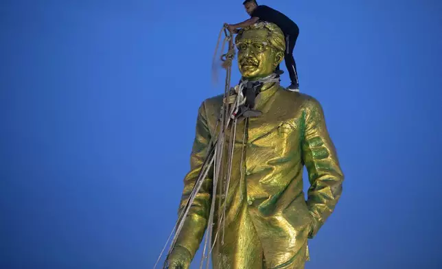 A man climbs to tie a rope around the head of a large statue of Sheikh Mujibur Rahman, father of Bangladesh leader Sheikh Hasina, as protesters try to bring it down after she resigned as Prime Minister, in Dhaka, Bangladesh, Monday, Aug. 5, 2024. (AP Photo/Rajib Dhar)