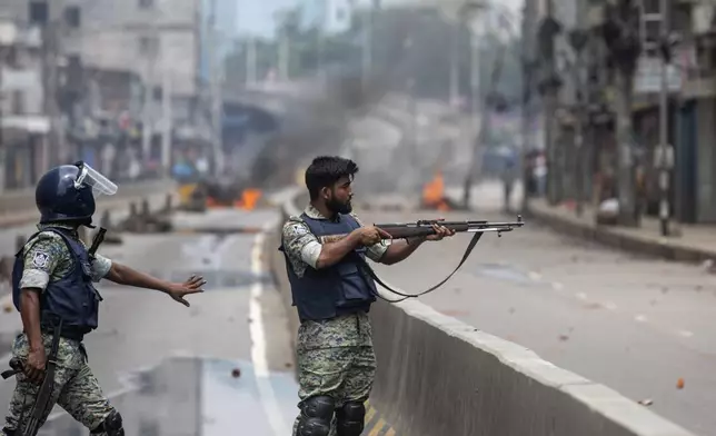 A policeman aims his weapon at protesters during a curfew imposed following violence during protests against Prime Minister Sheikh Hasina and her government, in Dhaka, Bangladesh, Monday, Aug. 5, 2024. (AP Photo/Rajib Dhar)