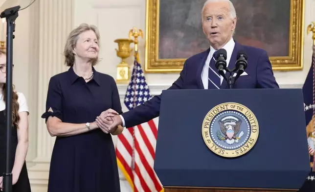 President Joe Biden, right, reaches out to hold hands with Elizabeth Whelan, left, as he delivers remarks on a prisoner swap with Russia from the State Dining Room of the White House, Thursday, Aug. 1, 2024, in Washington. Elizabeth Whelan's brother, Paul Whelan, was part of the prisoner swap. (AP Photo/Evan Vucci)