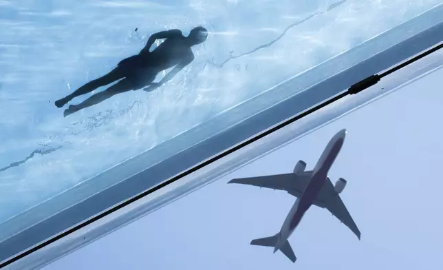 A swimmer in the Sky Pool, a transparent swimming pool suspended 35 meters above ground between two apartment buildings, is in the water during hot weather in central London, Monday August 12, 2024. (James Manning/PA via AP)