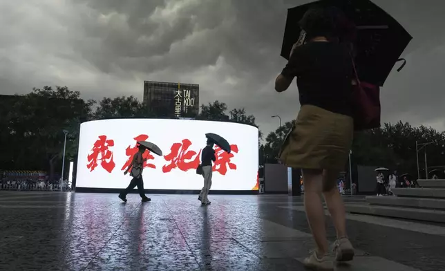 People walk past a sign which reads "I'm in Beijing" during a sudden rain storm in Beijing, Friday, Aug. 23, 2024. (AP Photo/Ng Han Guan)