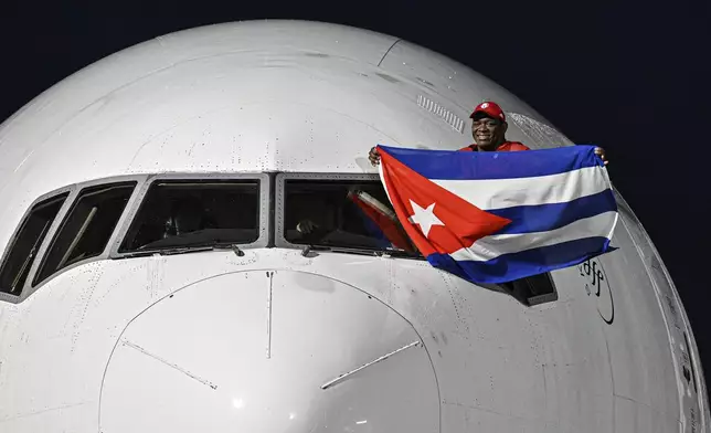 Cuban wrestler Mijain Lopez Nunez, a five-time Olympic champion, waves a Cuban flag from the pilot's window of a plane as he arrives at Jose Marti airport in Havana, Cuba, Monday, Aug. 12, 2024. (Adalberto Roque/Pool Photo via AP)