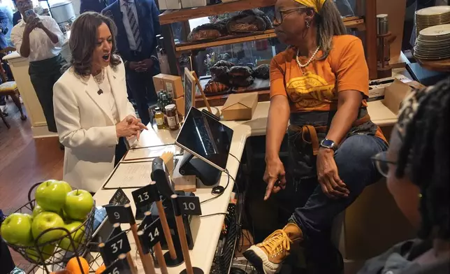 Democratic presidential nominee Vice President Kamala Harris looks at an employees shoes during a stop at Dottie's Market in Savannah, Ga., Thursday, Aug. 29, 2024. (AP Photo/Jacquelyn Martin)